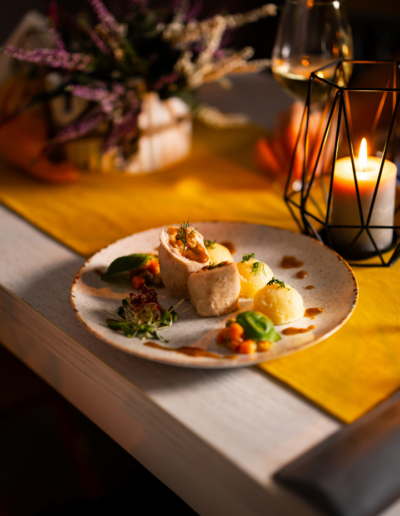 Elegancko zaserwowane danie obiadowe z roladką mięsną, purée ziemniaczanym i sosem, przytulna atmosfera ze świecą w restauracji