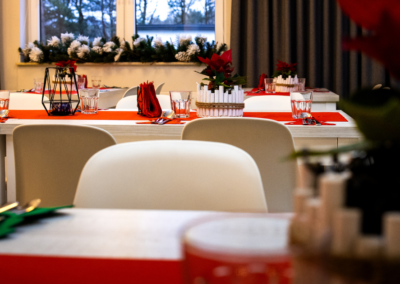Pięknie nakryty stół wigilijny w restauracji Hotelu Jurajski Kryształ, ozdobiony czerwonymi poinsecjami w rustykalnych doniczkach, geometrycznymi lampionami i oświetloną choinką w tle. Gotowy na uroczystą kolację świąteczną w Jurze.