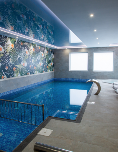 Kryty basen z błękitną mozaiką i ozdobną ścianą w liście palmowe w strefie wellness Hotelu Jurajski Kryształ