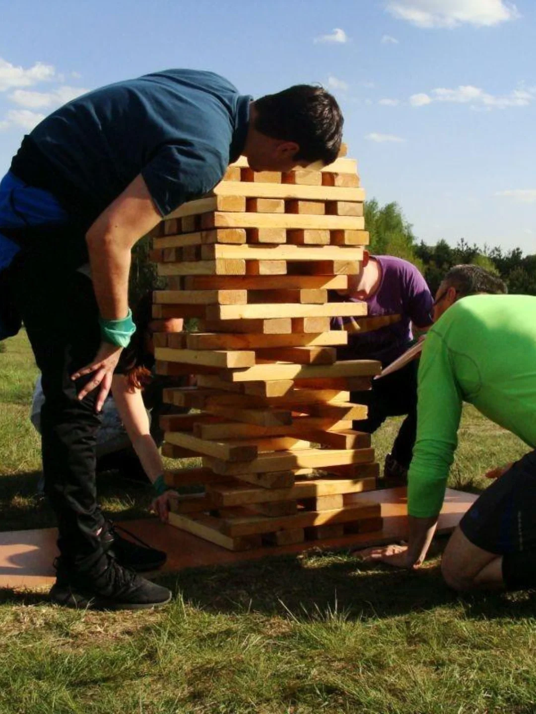 Grupa osób grająca w dużą plenerową wieżę Jenga