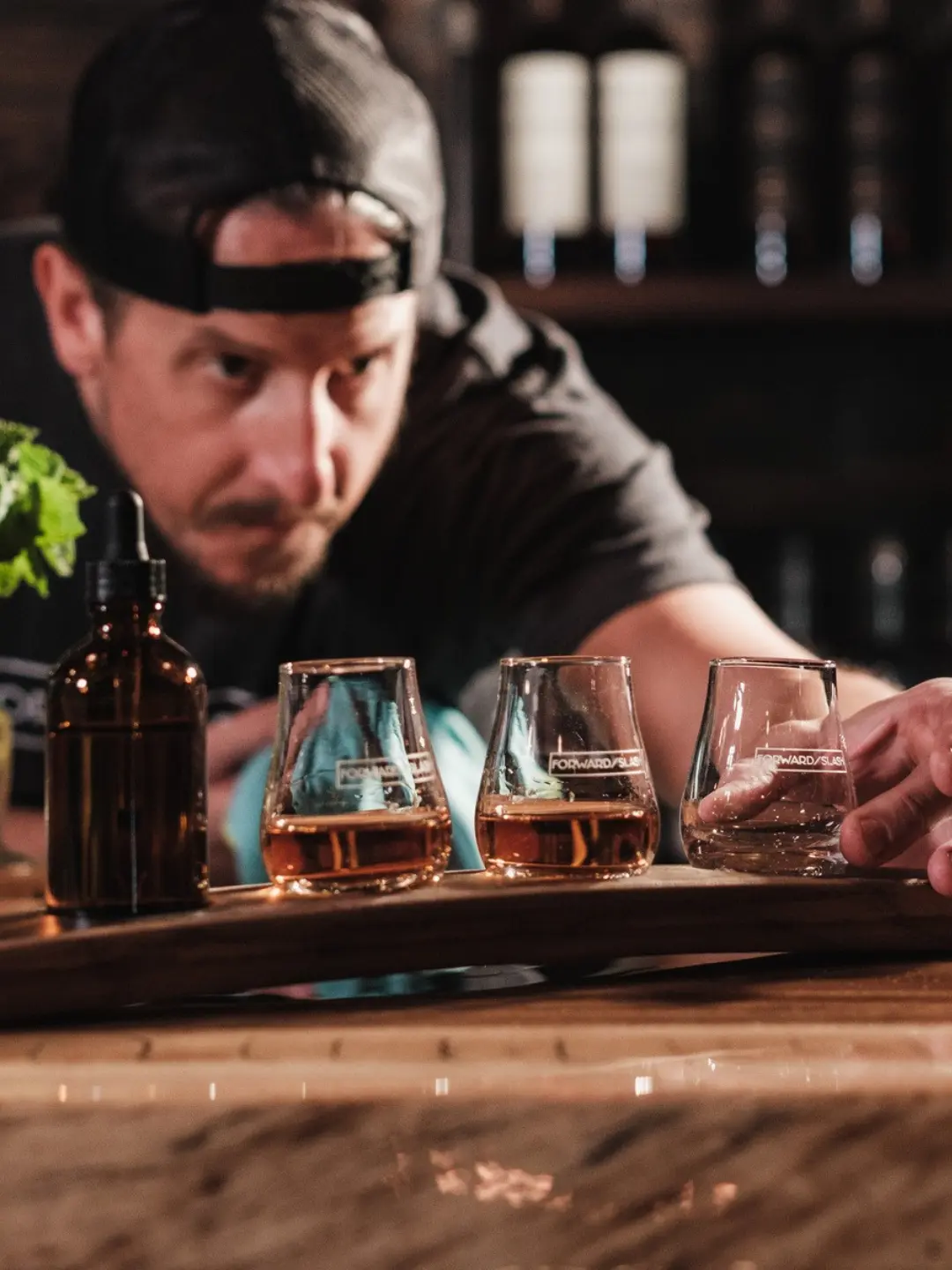 Trzy degustacyjne szklanki z whisky ustawione na drewnianym panelu barowym