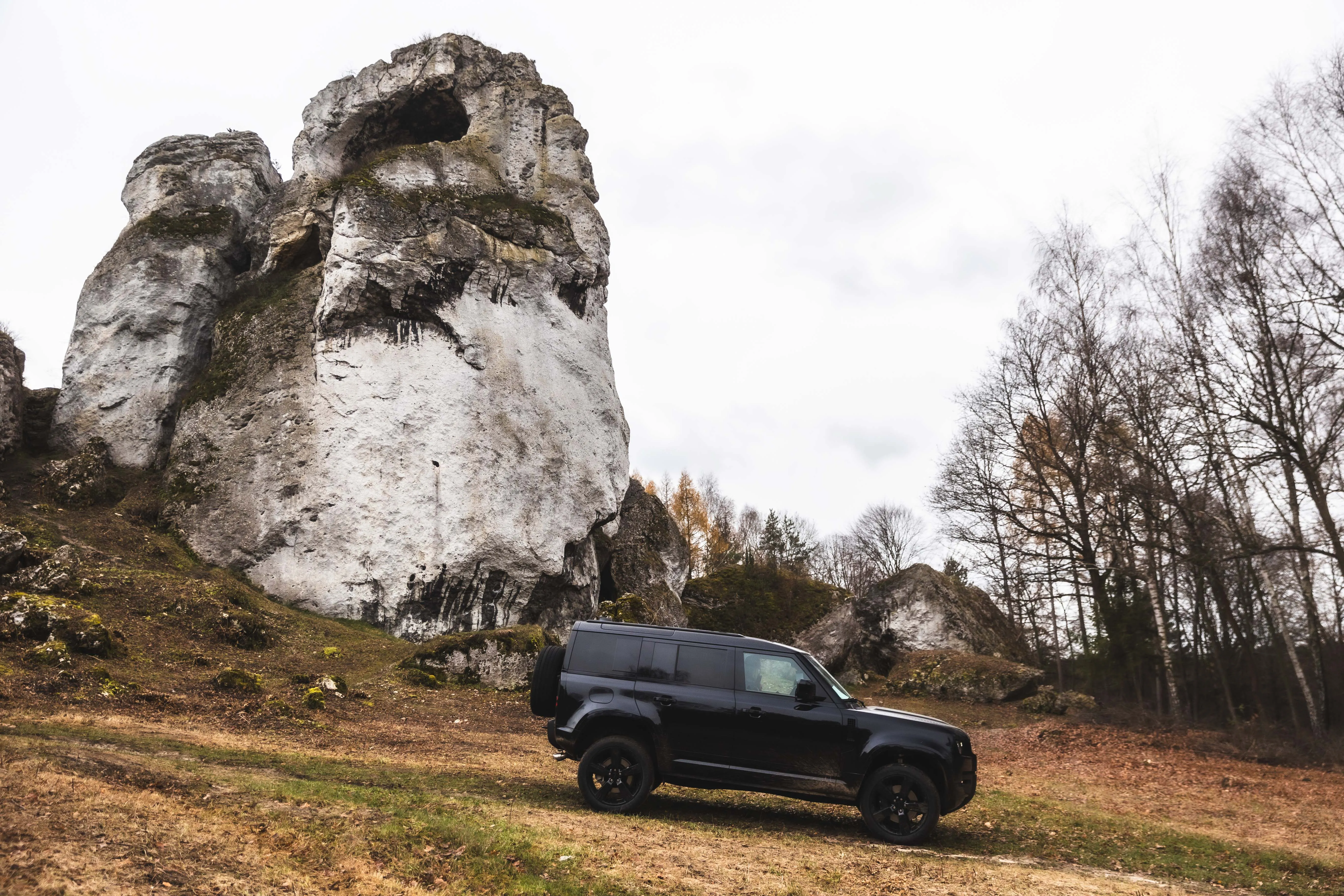 Czarny samochód terenowy Land Rover Defender na trawiastym wzniesieniu obok wysokich skał