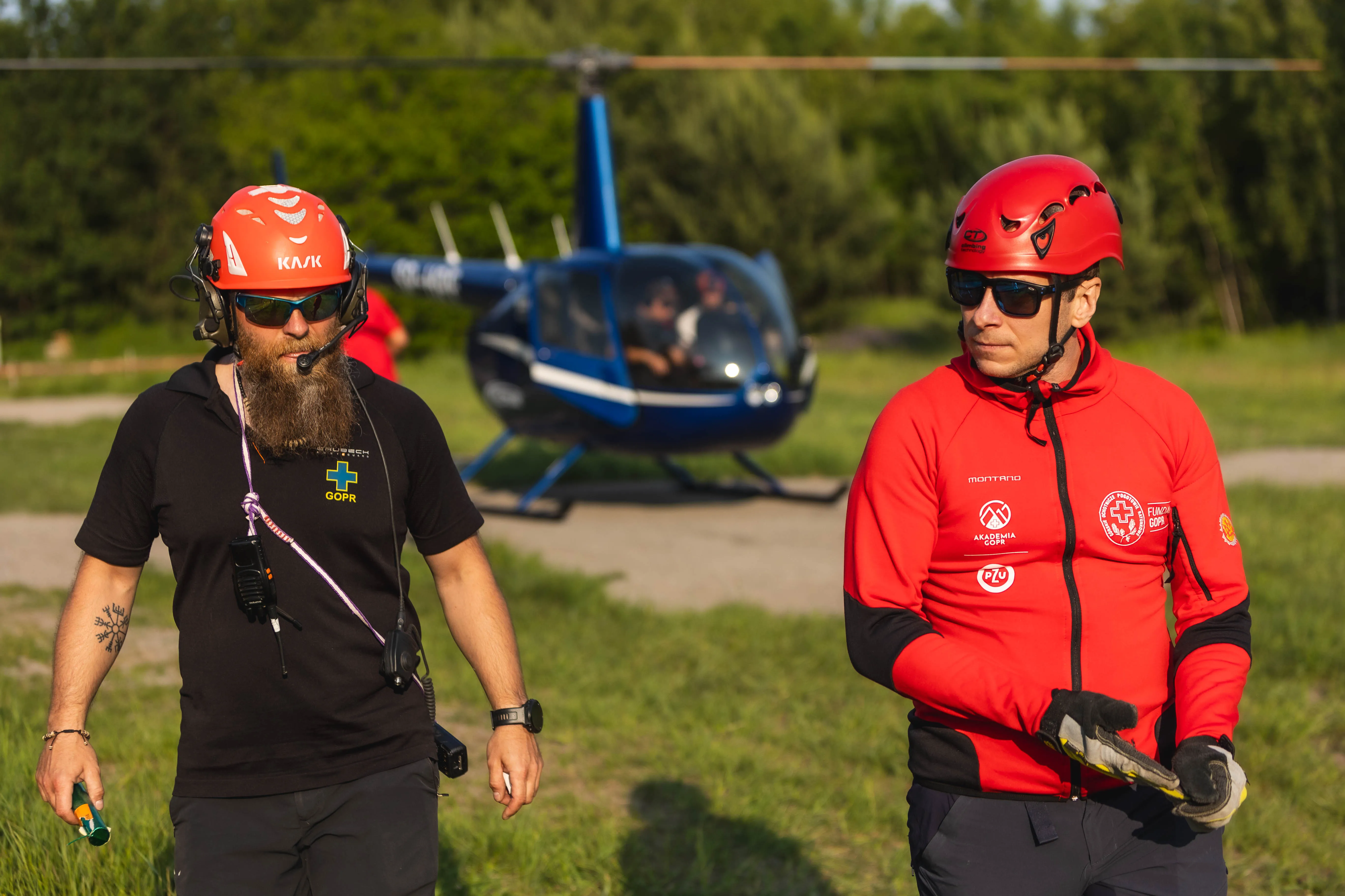 Dwaj ratownicy GOPR w kaskach i odzieży technicznej na tle niebieskiego helikoptera