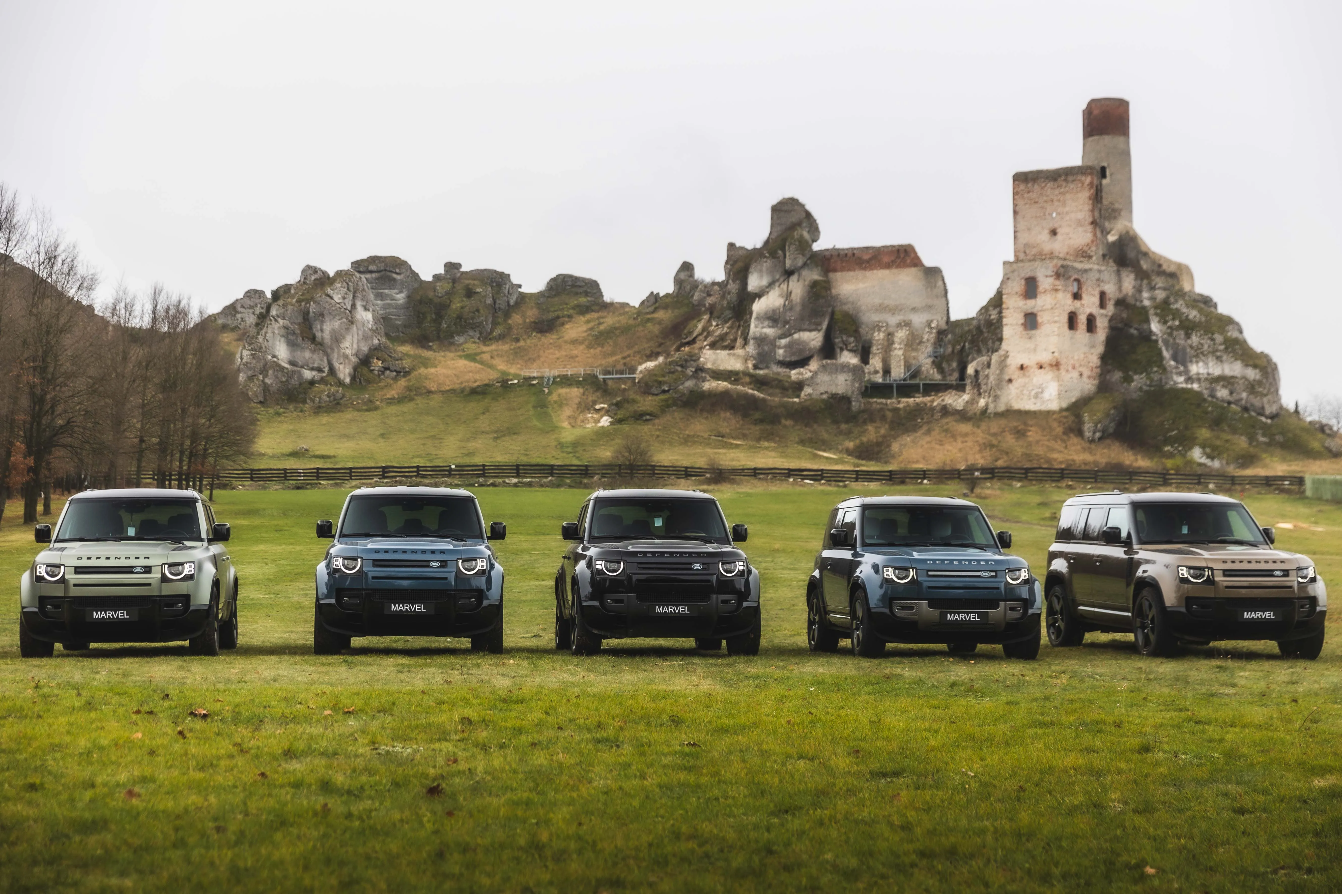 Rząd pięciu nowych modeli Land Rover Defender na zielonej trawie przed ruinami zamku